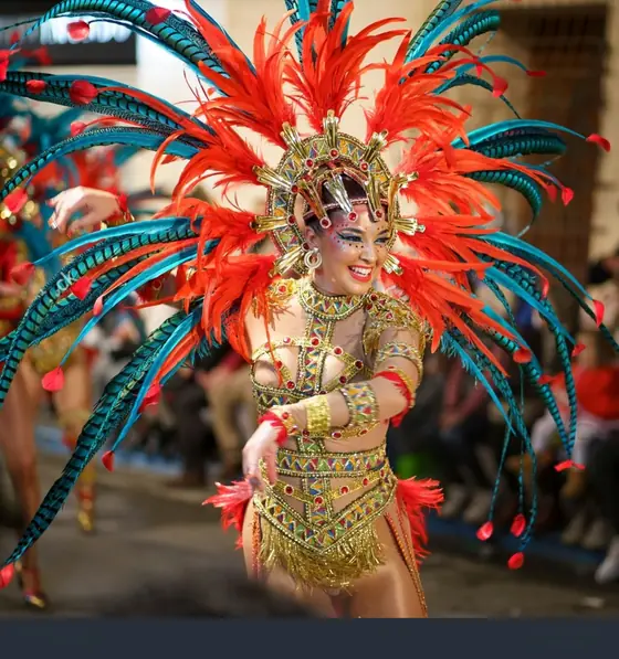 Una comparsista del Carnaval de Águilas desfilando, con un tocado de plumas rojas y turquesas y un traje bordado de lentejuelas