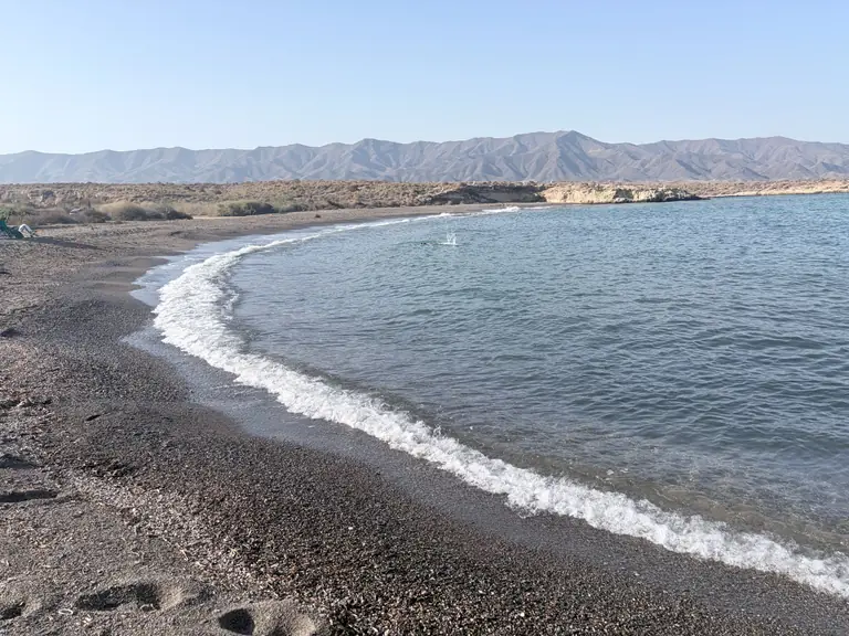 Playa del Saladar con luz baja: la orilla de grava oscura curvándose y la Sierra de la Almenara al fondo