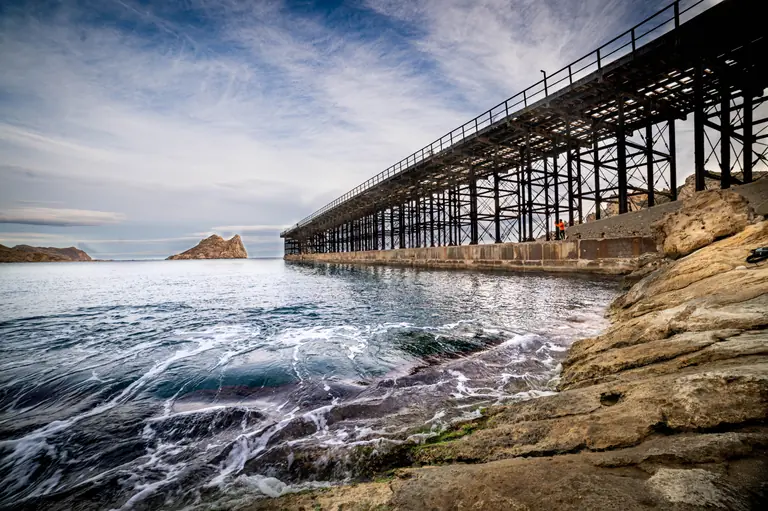 El embarcadero del Hornillo visto desde las rocas, con el oleaje entrando en la cala y la isla del Fraile en el horizonte