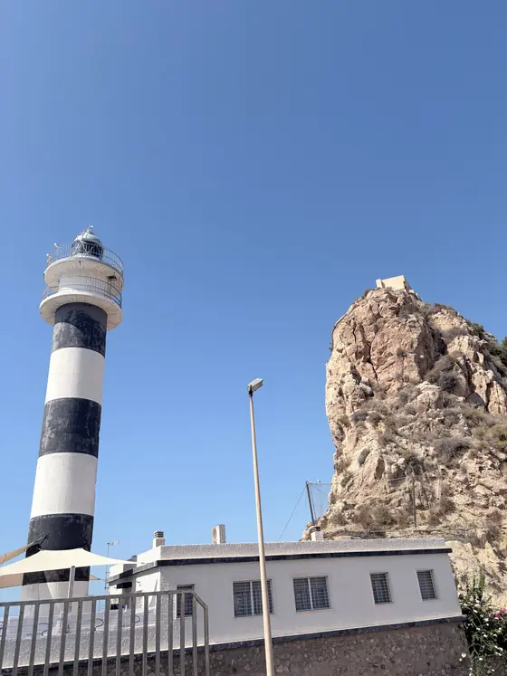 El faro de Águilas, con sus franjas blancas y negras, y la roca del cabo detrás