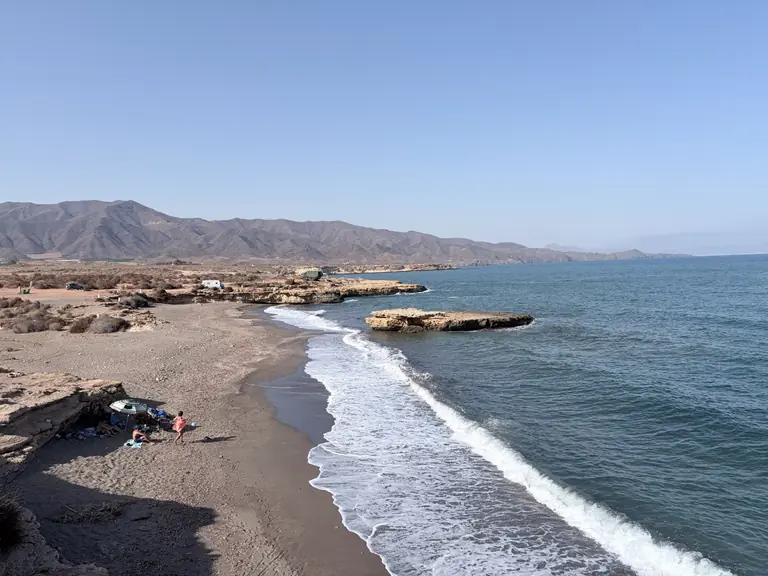 La playa de La Galera vista desde lo alto, con una mesa de roca dentro del agua y la sierra detrás