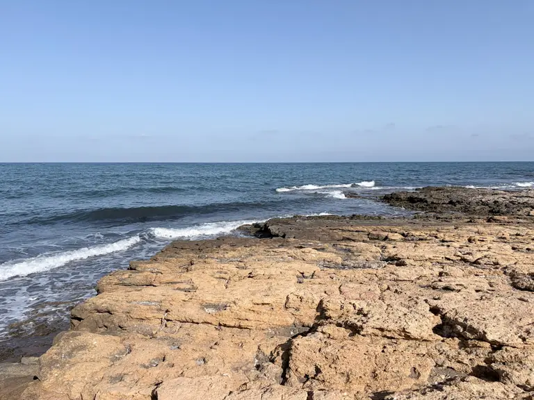 La laja dorada de Cala de los Abejorros metiéndose en el mar, con la espuma rompiendo en el borde