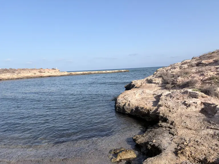 Cala del Pozo de las Huertas, recogida entre paredes de roca clara, con la sierra al otro lado del agua