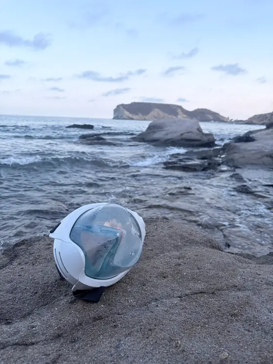 Una máscara de snorkel apoyada en la roca al atardecer, con el mar y la Isla del Fraile detrás