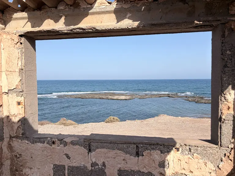 El hueco de una ventana en una construcción en ruina, con el arrecife y el mar abierto enmarcados dentro